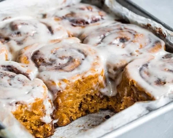 Freshly baked gluten-free pumpkin cinnamon rolls topped with cream cheese frosting